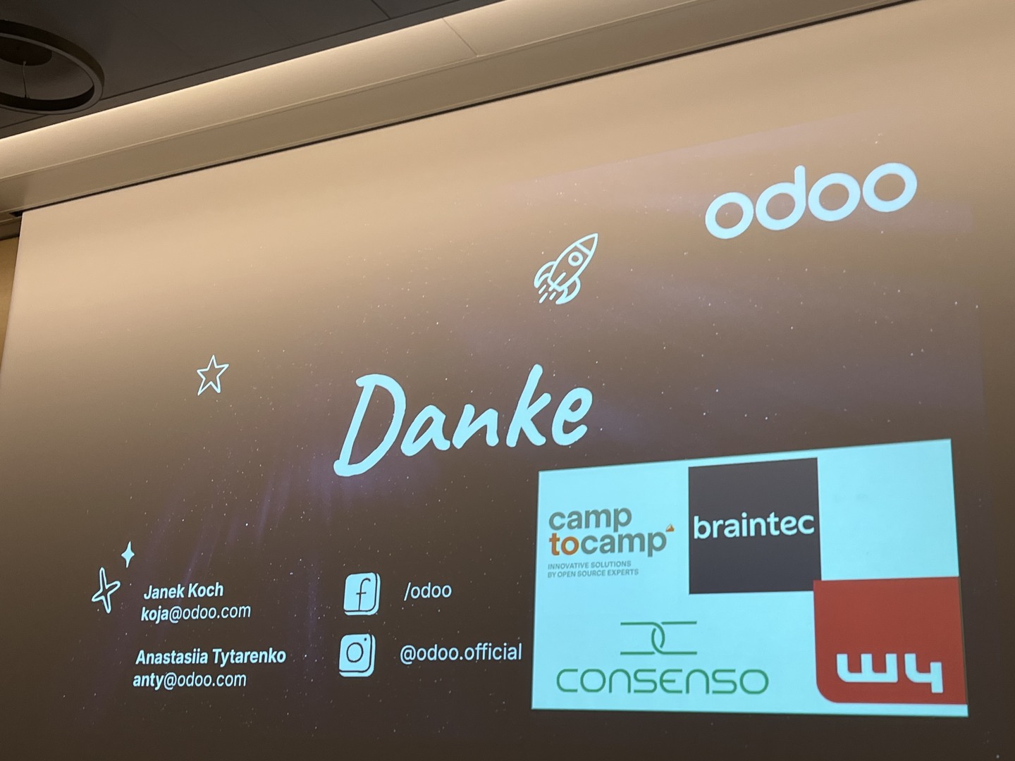 Eine Präsentationsfolie mit einem dunklen Sternenhintergrund, auf der in grosser Schrift „Danke“ steht. Sie zeigt das Odoo-Logo, Social-Media-Handles, Kontaktdaten für zwei Personen und ein Raster mit Partner-Logos von camp to camp, braintec, consenso und w4.